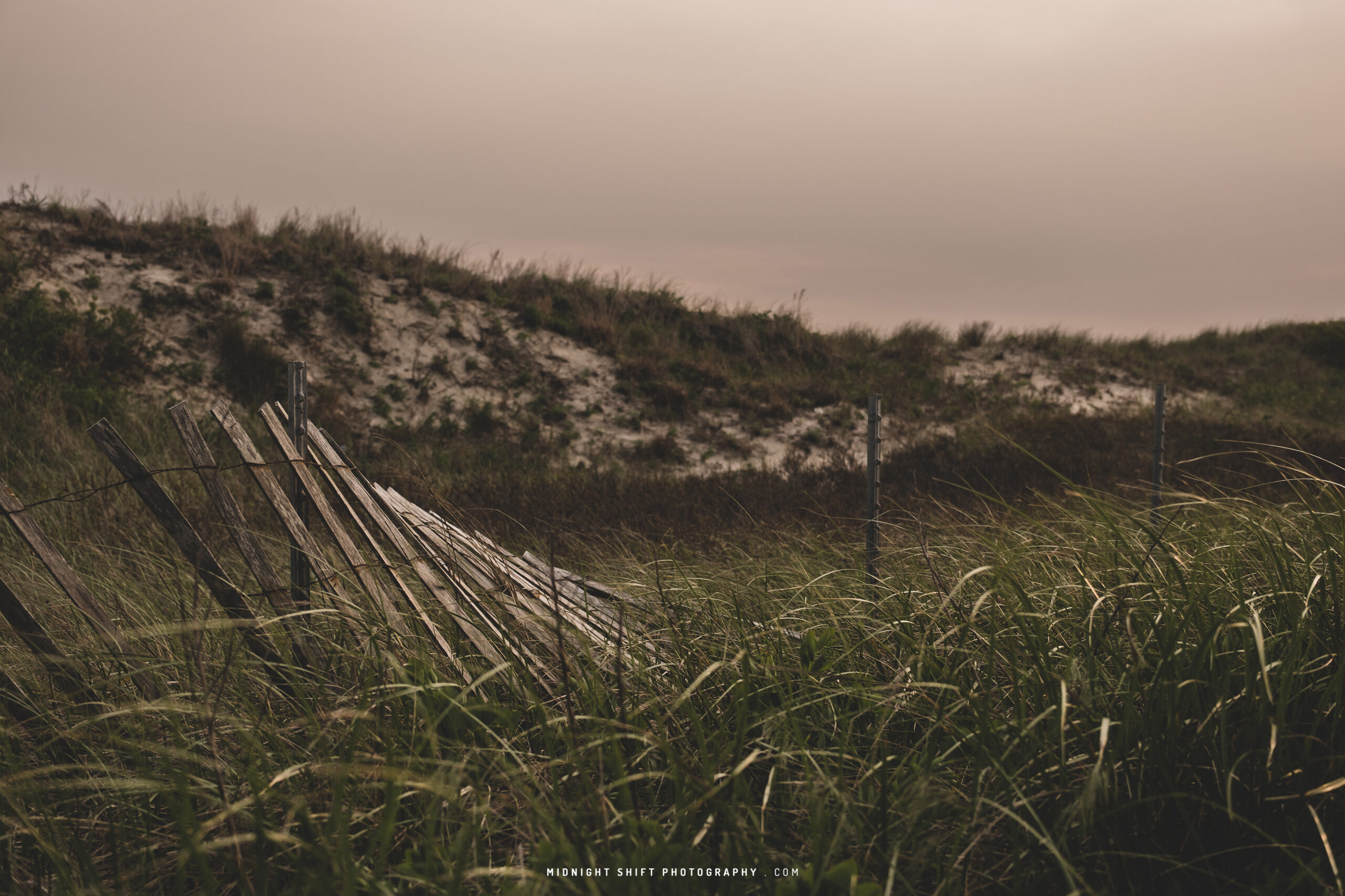 A partially fallen beach fence in some sand dunes at Horseneck Beach in Westport, Massachusetts